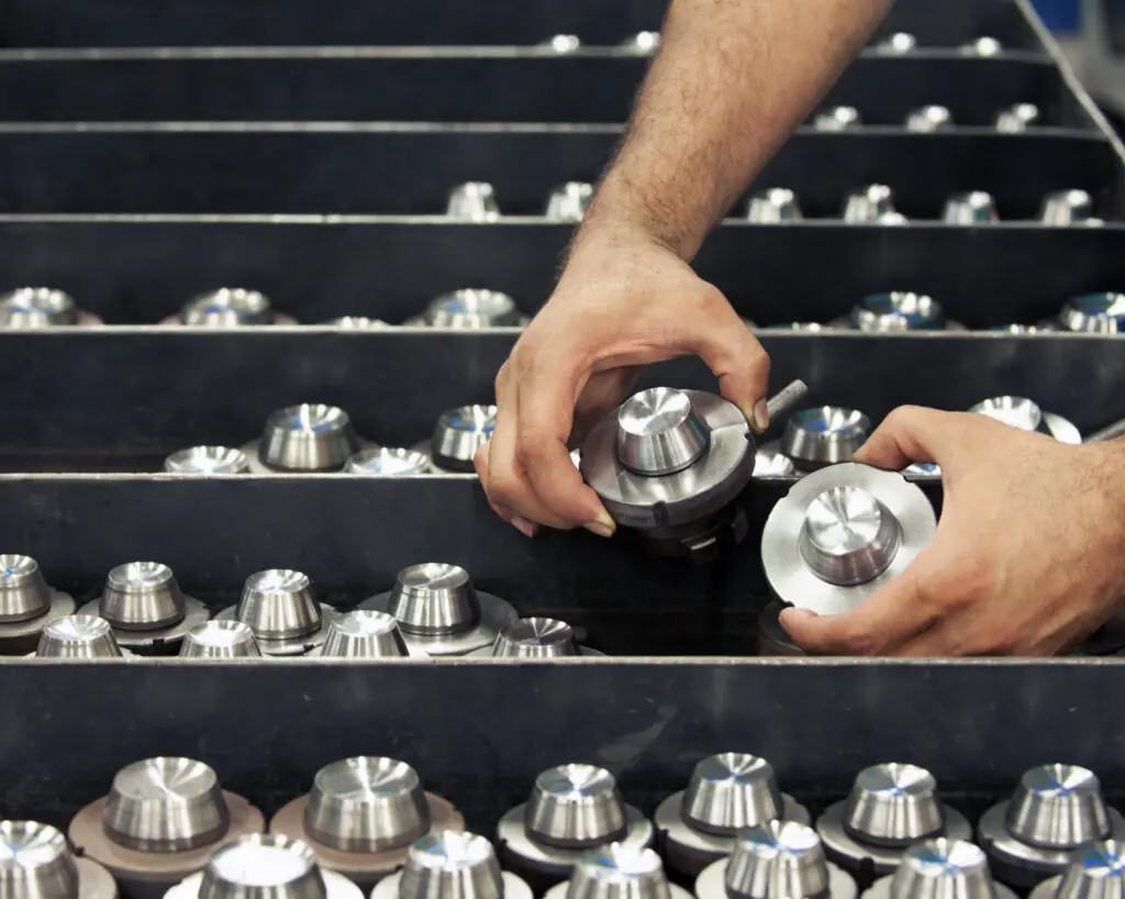 Hands inspecting metal parts in factory.