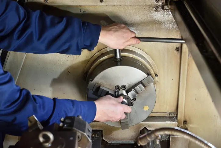 Technician adjusting a metal lathe's tool post with a wrench.