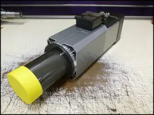 A compact gray industrial motor with a yellow protective cap on the shaft.