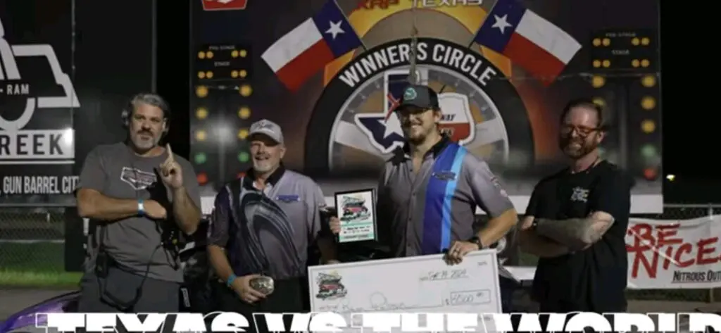 Two men in a winner's circle holding a trophy and a large check.