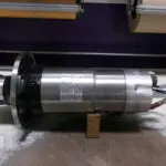 A cylindrical metallic industrial component resting on a wooden block.