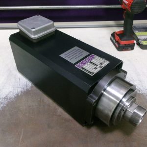 A black industrial spindle motor with a label and metallic front part on a workbench.