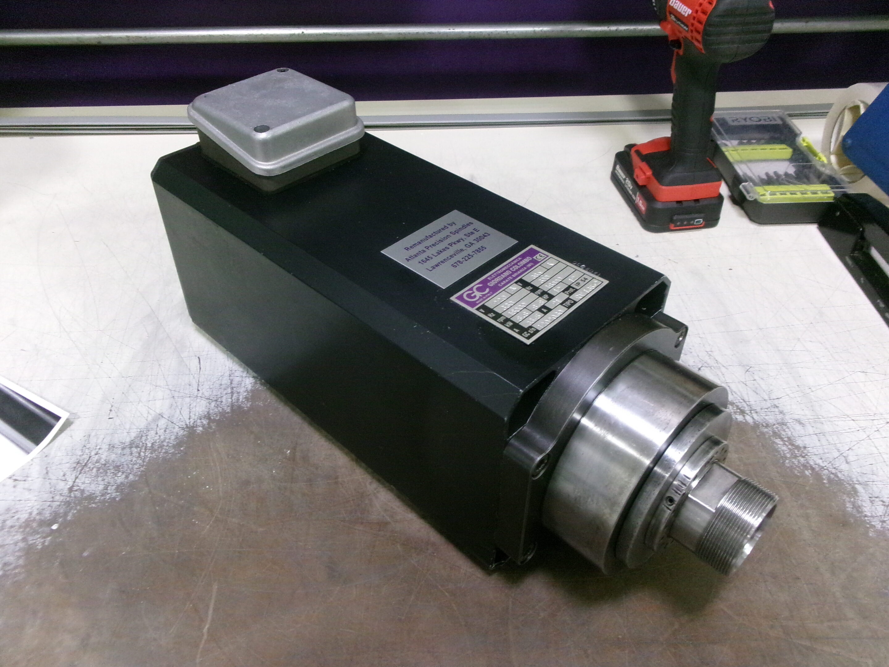 A black industrial spindle motor with a label and metallic front part on a workbench.