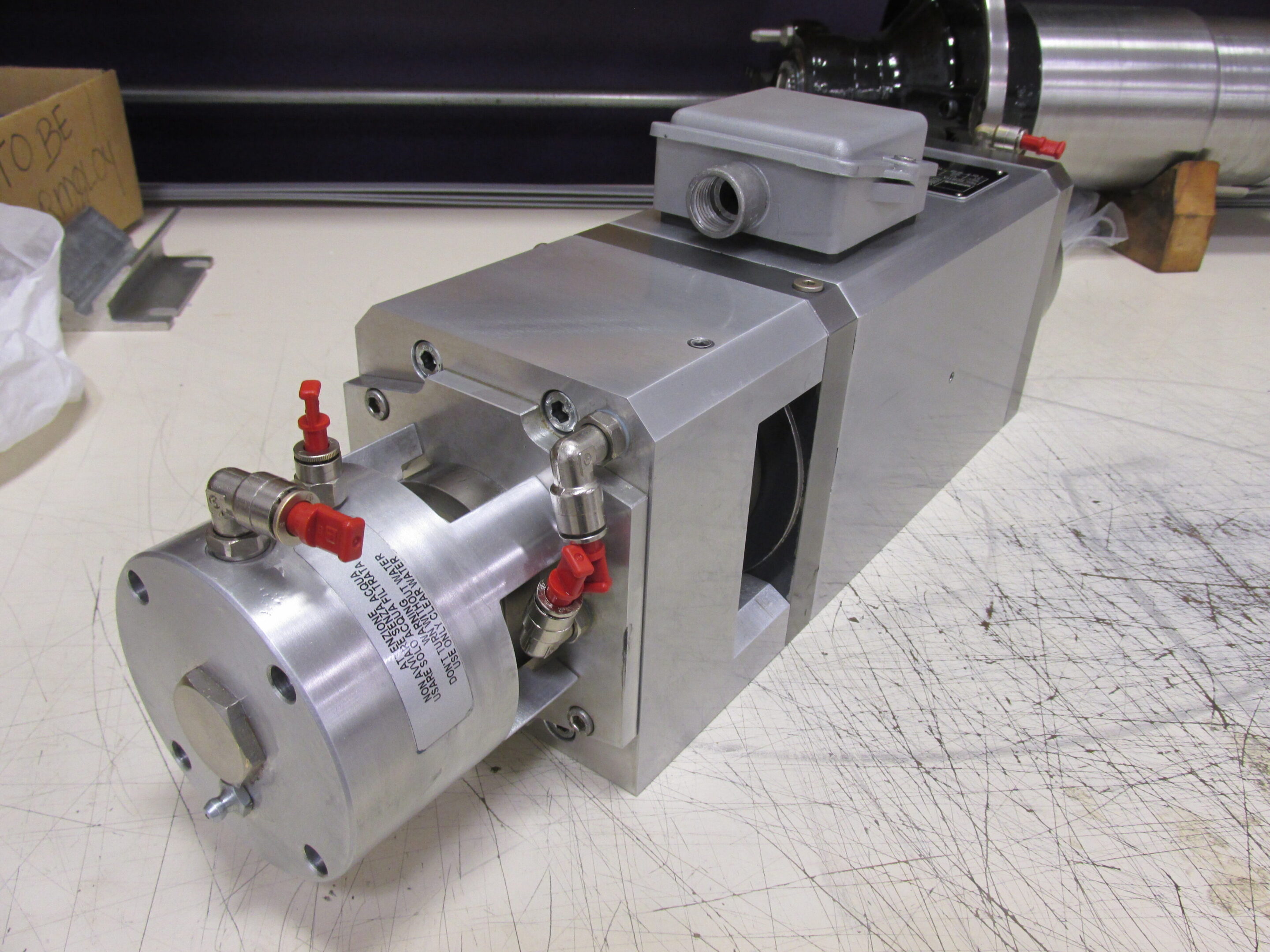 Metal industrial machine component with red valves on a workbench.