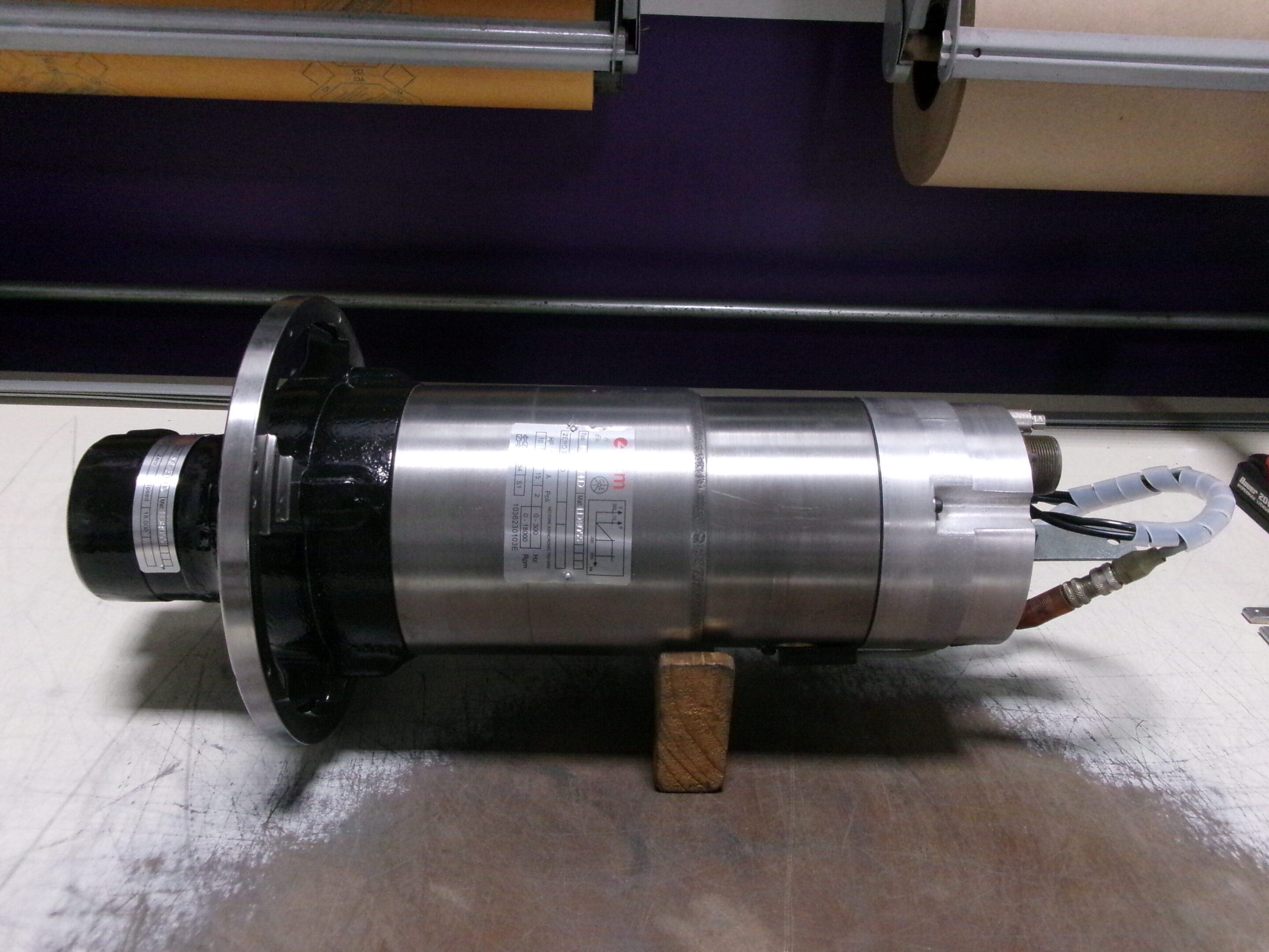 A cylindrical metallic industrial component resting on a wooden block.